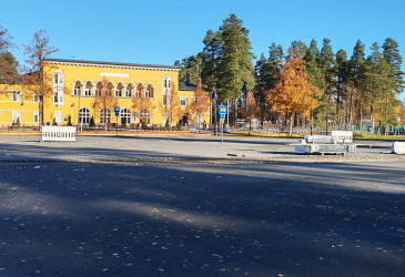 Parkkialue, jonka takana näkyy keltainen kouluraknneus.