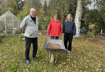 Puseniukset seisomassa pihalla, yhdellä kottikärryt kädessä.