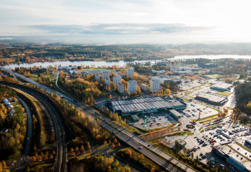 Ilmakuvassa näkymä Imatran Mansikkalaan, jossa rautatie, valtatie ja kauppakeskuksia, taustalla Vuoksi.