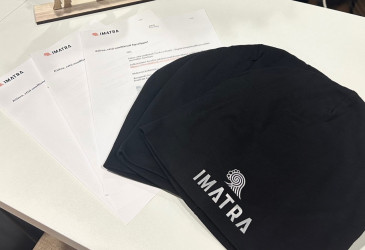 Pöydällä mustia Imatra-pipoja ja kaupungin logolla varustettuja kirjeitä.