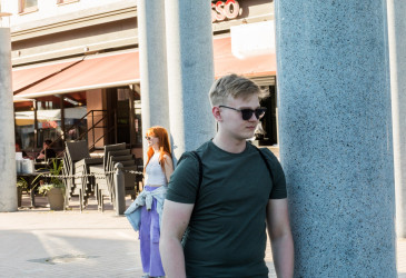 Poika pylvään juurella kadulla, taustalla tyttö.
