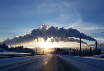 Tehtaan savut taivaalla auringon laskiessa.