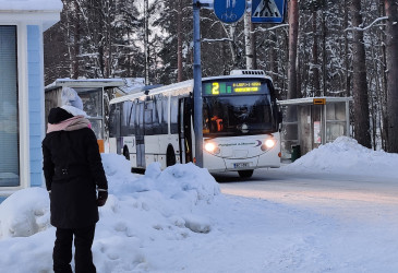 Bussi pysäkillä ja saattaja seuraa bussin lähtöä.
