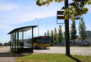 Linja-auto ajaa bussipysäkin ohi aurinkoisessa säässä.