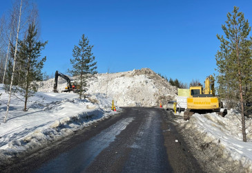 Lumenkaatopaikalla kaivinkone ja iso kasa lunta kevätauringossa.