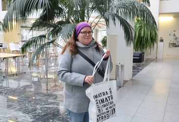 Jenni Könönen kaupungintalon aulassa Imatra-tuotekassi kädessään.