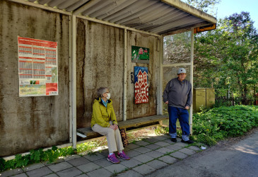 pysäkkikatos ja kaksi bussia odottavaa ihmistä.