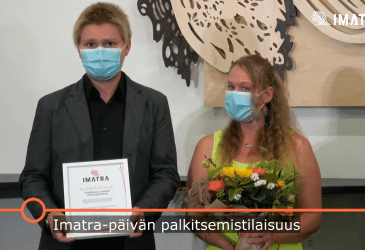 Mies ja nainen maskeissa, kunniakirja ja kukat kädessä.