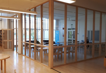 Olohuoneen pöydät, sohvat ja tuolit on erotettu muusta kirjastotilasta lasiseinin.