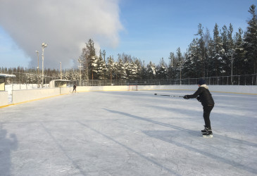 Kaksi luistelijaa kaukalossa aurinkoisessa talvisäässä.