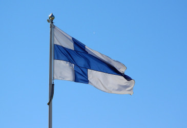 Suomen lippu heiluu tuulessa sinistä taivasta vasten.