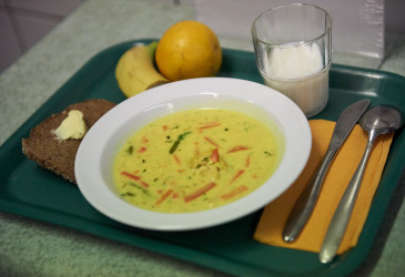 Keittolautanen tarjottimella. Tarjottimella myös leipä, hedelmiä, maitolasi sekä ruokailuvälineet.