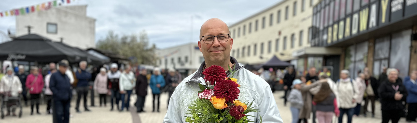 Mies seisoo kävelykadulla kukkakimppu ja kunniakirja käsissään.