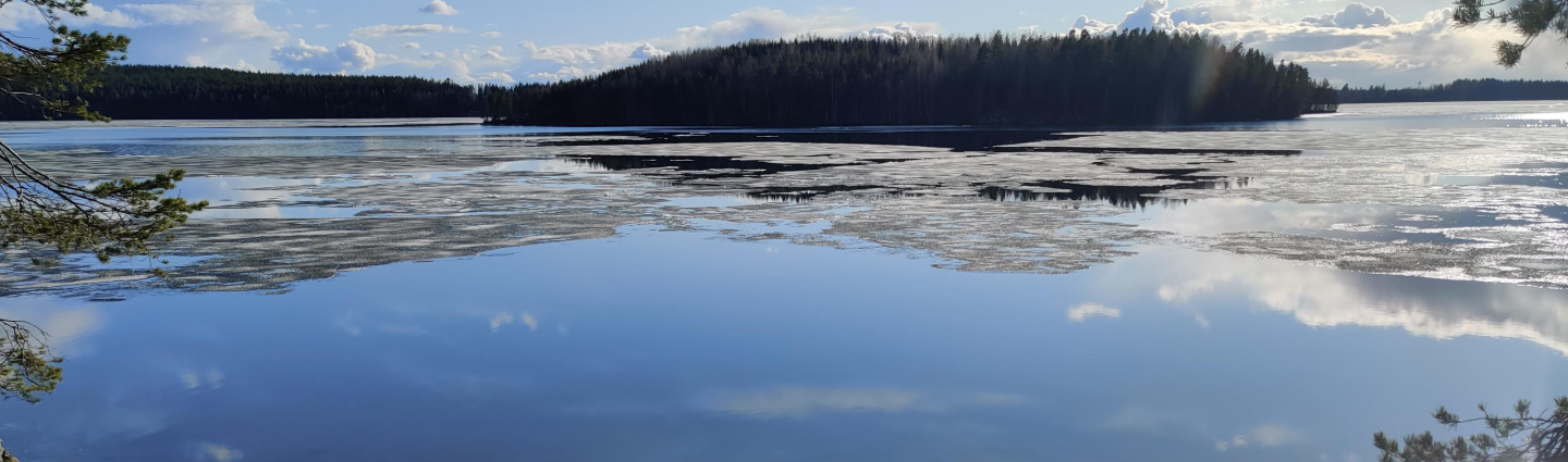 Viimeiset jäät sulamassa tyynen järven pinnasta auringonpaisteessa.