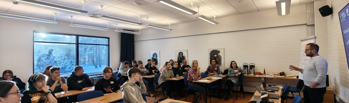 Ihmisiä luentosalissa kuuntelemassa luennoitsijaa.