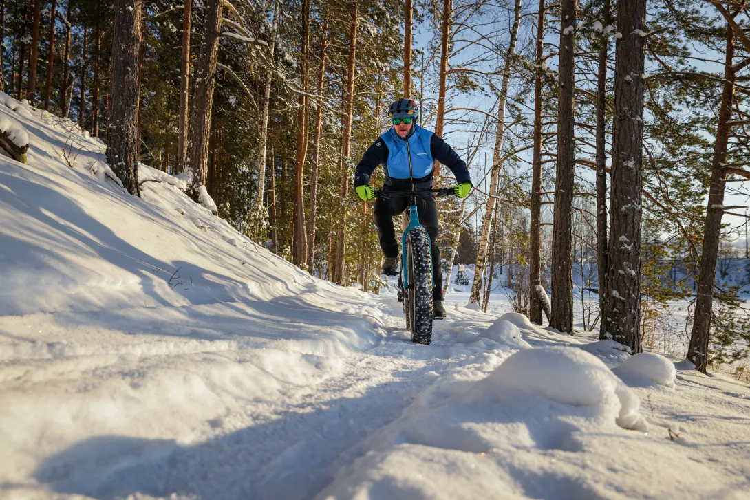 Maastopyöräilijä talvimaisemassa. Aurinko paistaa.