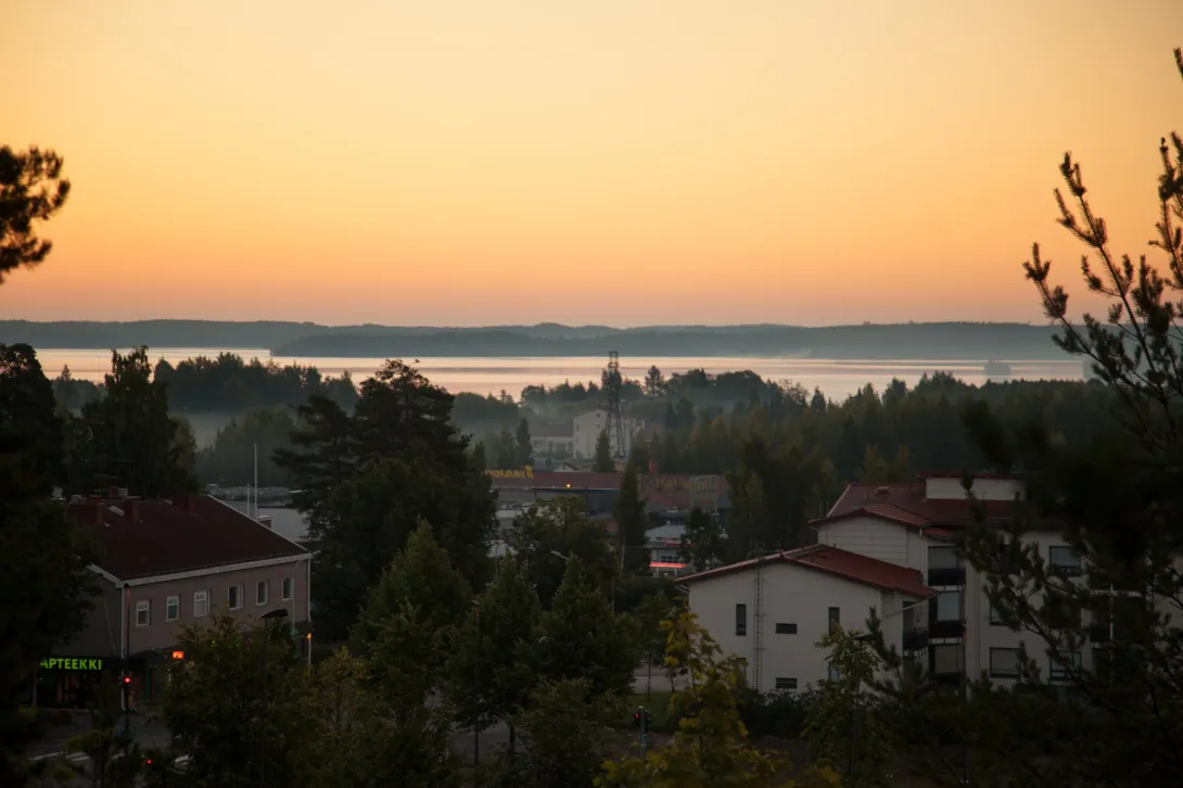 Maisemakuva Vuoksenniskalta ilta-auringon aikaan. Kuvassa etualalla taloja ja takana siintää järvi.
