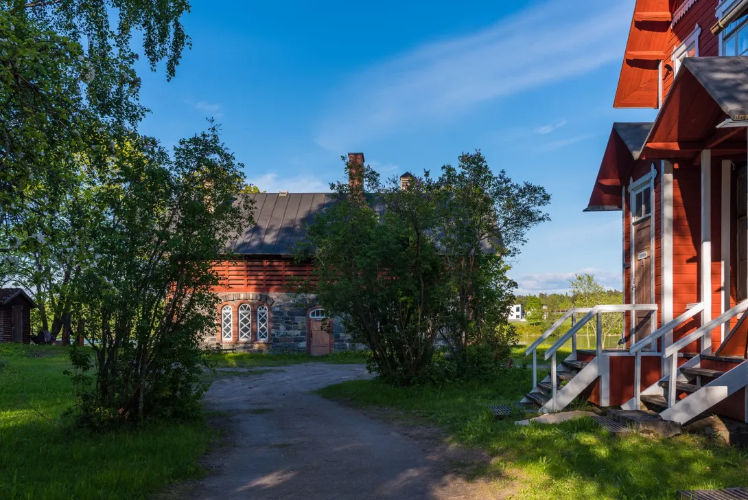 Kesäinen kuva, jossa hiekkatie kulkee keskellä punaisia, vanhoja puutaloja.