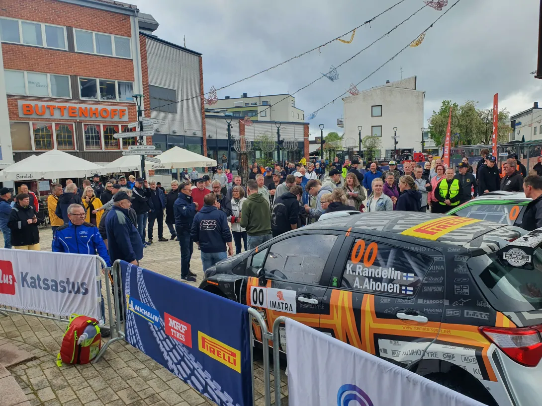 Ralliauto ja ihmisiä keskustassa.